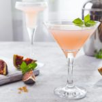 Sparkling pink lemonade martini with figs and honey on light background over windows