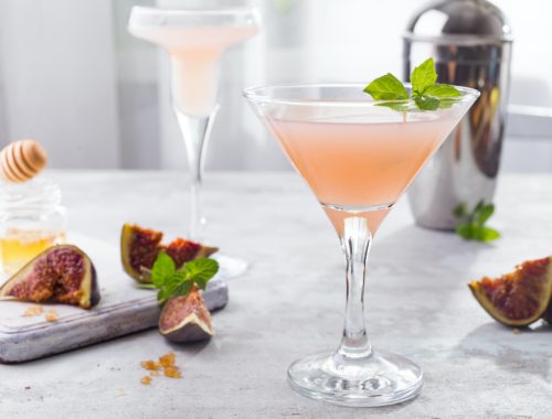 Sparkling pink lemonade martini with figs and honey on light background over windows