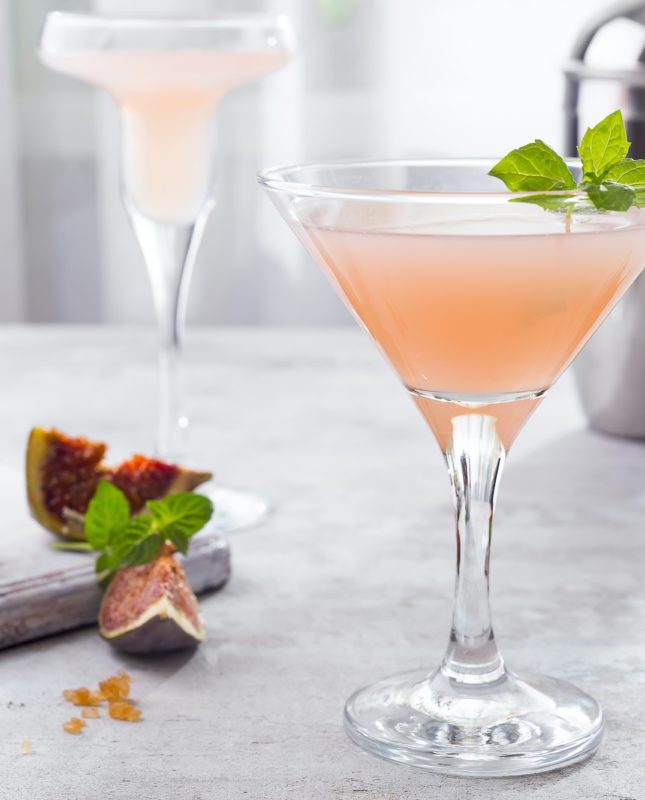 Sparkling pink lemonade martini with figs and honey on light background over windows