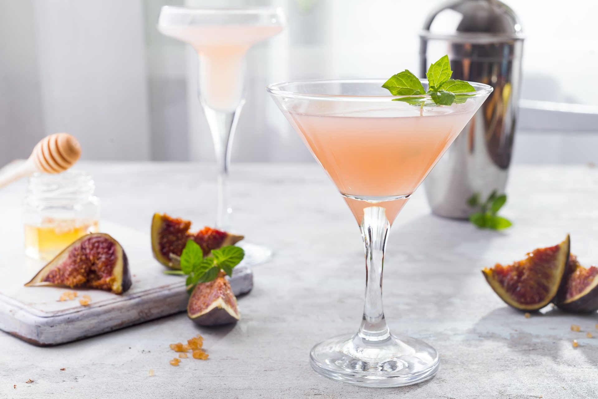 Sparkling pink lemonade martini with figs and honey on light background over windows