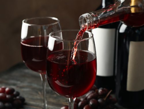 Wine is poured from a bottle in glass on wooden table, close up