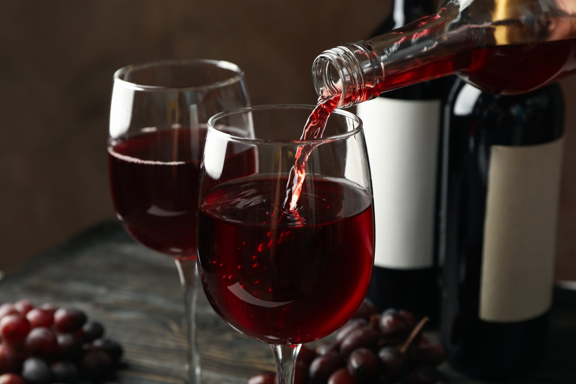 Wine is poured from a bottle in glass on wooden table, close up